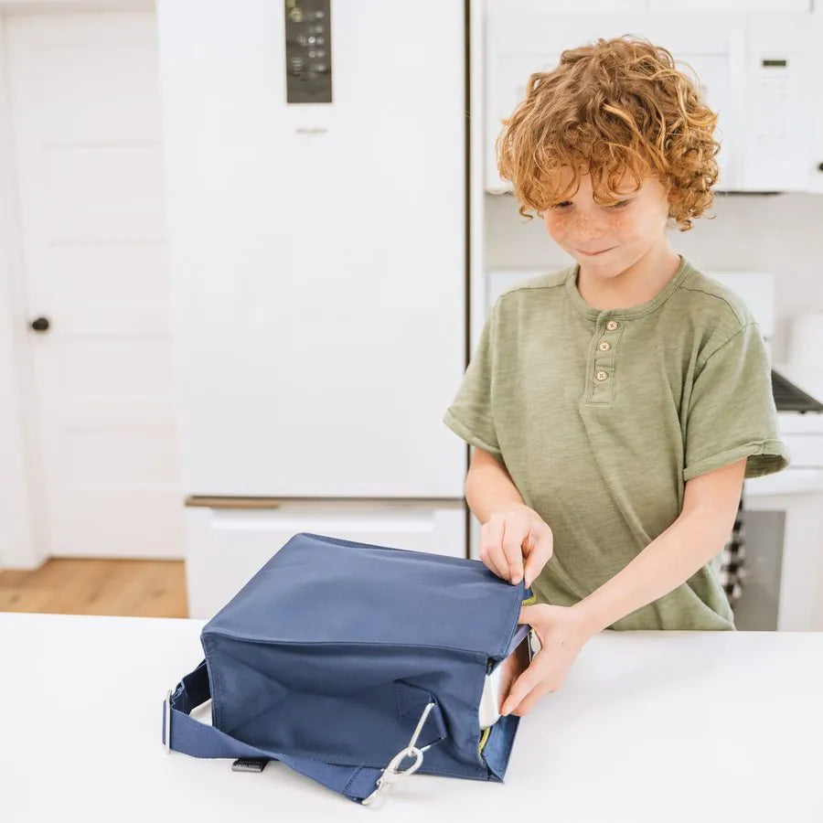 A boy packing his navy recycled insulated lunch tote in the kitchen