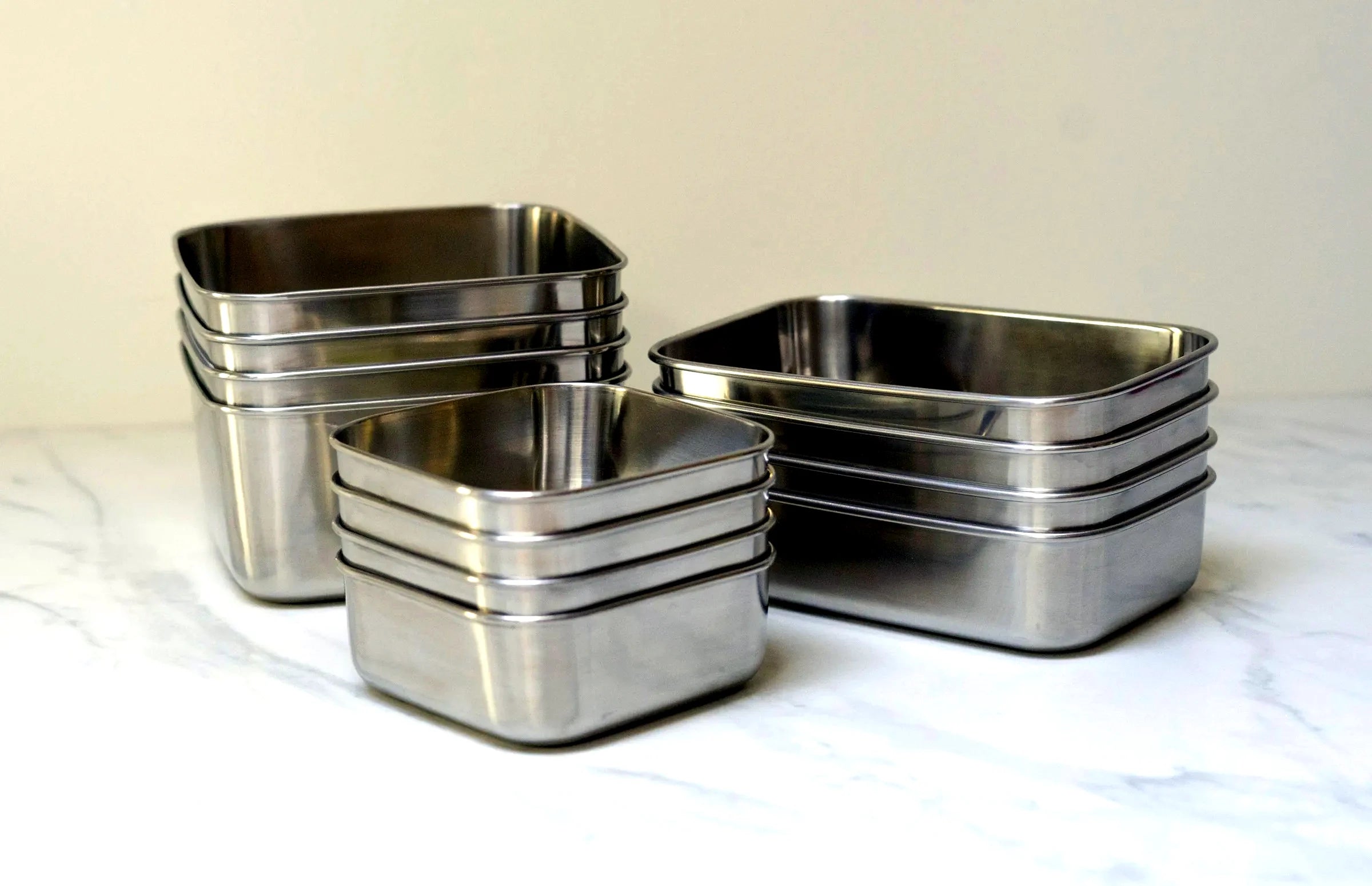Stainless steel square and rectangle containers nested in stacks on a marble bench