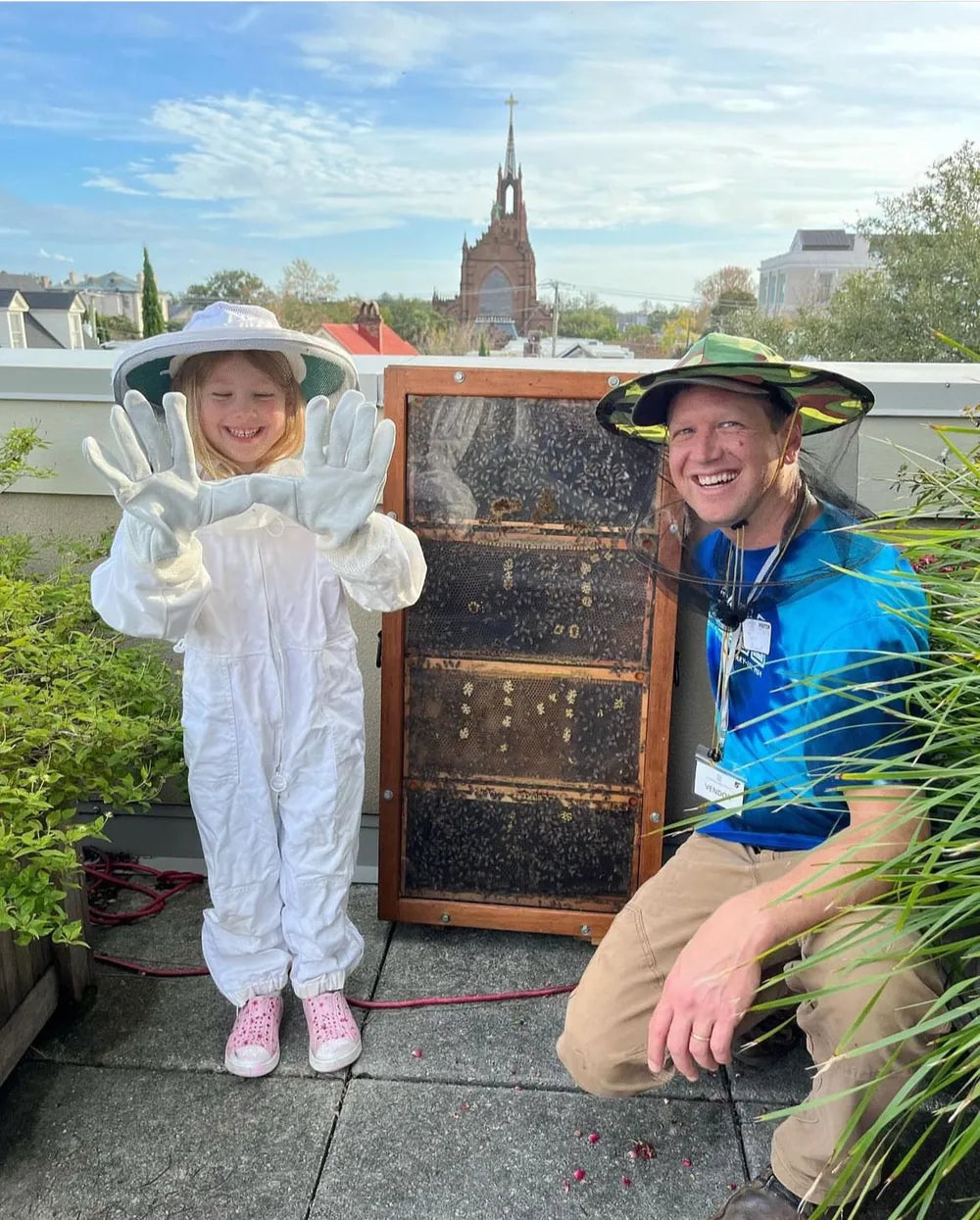 A smiling child in a bee suit beside an observation beehive